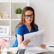 woman-in-glasses-reading-newspaper-at-office-PQKZVRF
